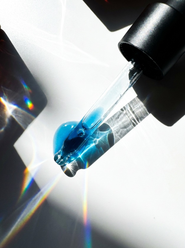 A drop of peptide serum falling from a glass dropper